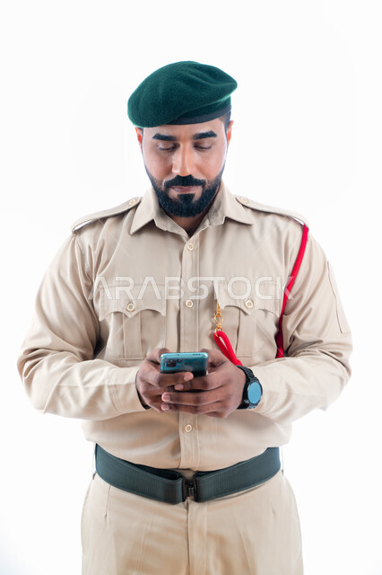 تصفح المواقع والتطبيقات الإخبارية، بورتريه لشرطي عربي إماراتي خليجي يرتدي بدلة الشرطة ويستخدم الهاتف المحمول، استخدام وسائل التواصل الإجتماعي، إدارة الأزمات والكوراث، تعزيز الأمن والأمان والثقة بالشرطة، الإستجابة لحالات الطوارئ، خلفية بيضاء