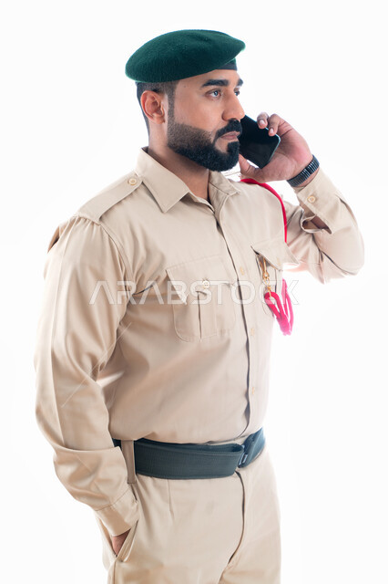 اجراء مكالمة من خلال الجوال، بورتريه لشرطي عربي إماراتي خليجي يرتدي بدلة الشرطة ويستخدم الهاتف المحمول، التواصل مع الأفراد، إدارة الأزمات والكوراث، تعزيز الأمن والأمان والثقة بالشرطة، الإستجابة لحالات الطوارئ، خلفية بيضاء