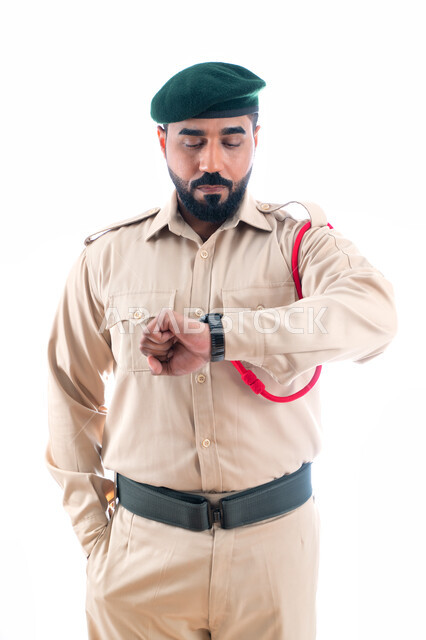 Setting appointments and knowing the time, a portrait of an Arab Emirati Gulf security man wearing a police suit and looking at the wristwatch, crisis and disaster management, enhancing security, safety and trust in the police, working to reduce crime rat