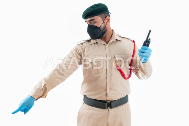 جمع المعلومات والأدلة للتحقق والتحري، التواصل مع فريف البحث وكشف الحقائق والجرائم  في موقع الجريمة من خلال جهاز الإرسال والإستقبال اللاسلكي، بورتريه لمحقق جنائي عربي خليجي إماراتي يرتدي بدلة الشرطة الرسمية ويشير بإصبع السبابة نحو شيء ما، خلفية بيضاء