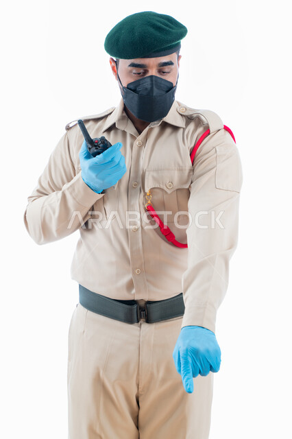 التواصل مع فريف البحث وكشف الحقائق والجرائم  في موقع الجريمة من خلال جهاز الإرسال والإستقبال اللاسلكي، بورتريه لمحقق جنائي عربي خليجي إماراتي يرتدي بدلة الشرطة الرسمية ويشير بإصبع السبابة نحو شيء ما، جمع المعلومات والأدلة للتحقق والتحري، خلفية بيضاء