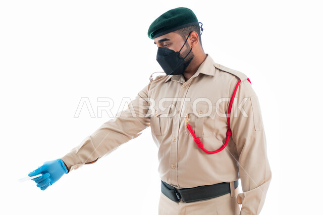 التأكد من المعلومات الشخصية لتفادي انتحال الشخصية، ارتداء الكمامة الواقية والقفازات، بورتريه لشرطي عربي خليجي إماراتي يرتدي زي شرطة دبي ويمسك بيده بطاقة الهوية للتأكد من المعلومات الشخصية للأشخاص في موقع الجريمة، خلفية بيضاء