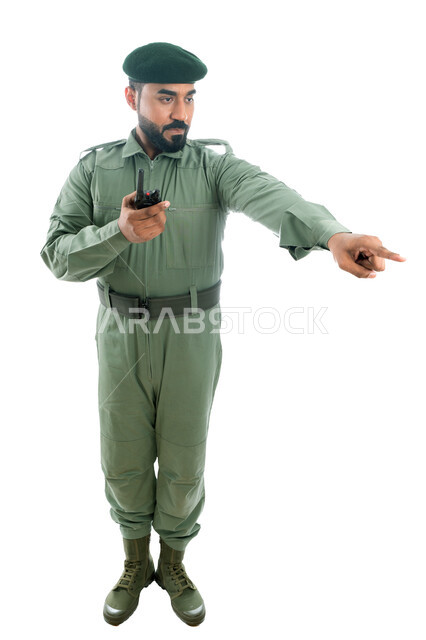 Finger movement and signals, emergency response, portrait of an Arab Gulf Emirati security man wearing a green security suit and using a wireless transceiver, index finger pointing towards something, full length body image, white background