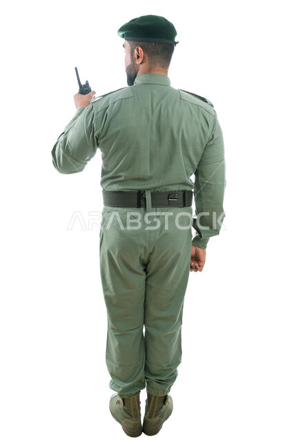 الوقوف بإستقامة وإستعداد وإنضباط، بورتريه من الخلف لرجل أمن عربي خليجي إماراتي يرتدي بدلة الأمن الخضراء ويستخدم جهاز الإرسال والإستقبال اللاسلكي، تعزيز الأمن والأمان والثقة بالشرطة، صورة الجسم بالطول الكامل، خلفية بيضاء