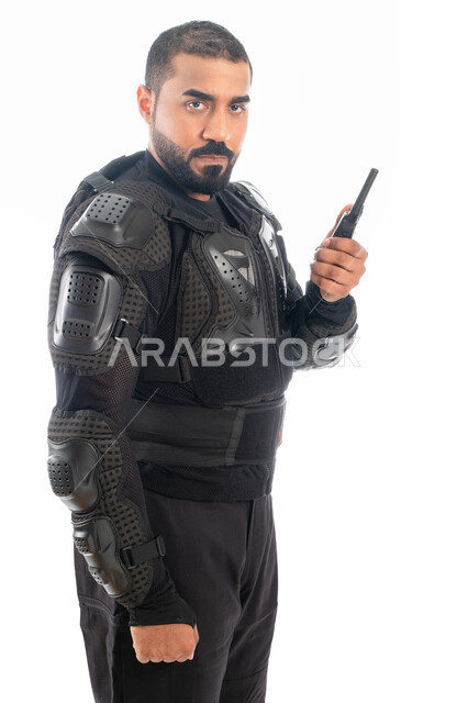 الوقوف باستقامة واستعداد وانضباط، بورتريه لشرطي عربي خليجي إماراتي من قوات التدخل السريع (سوات) يرتدي البدلة العسكرية السوداء ويستخدم جهاز الارسال والاستقبال اللاسلكي، الحفاظ على الأمن والأمان، خلفية بيضاء