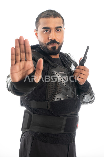 الحفاظ على الأمن والأمان، بورتريه لشرطي عربي خليجي إماراتي يرتدي البدلة العسكرية السوداء ويستخدم جهاز الارسال والاستقبال اللاسلكي ويشير بإشارة قف، قوات التدخل السريع (سوات)، إيماءات يدين تدل على التوقف والإنتظار، حركة يد وإشارات، خلفية بيضاء