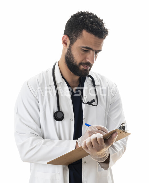 تقديم خدمات العلاج للمرضى بكل كفاءه ,بورتريه لطبيب سعودي يقوم بتدوين نتائج الفحوصات الطبية بالسجل الطبي ، شاب عربي اماراتي خليجي يرتدي المعطف الطبي و يقوم بإعداد التقارير الطبية ، العمل في القطاع الصحي، خلفية بيضاء