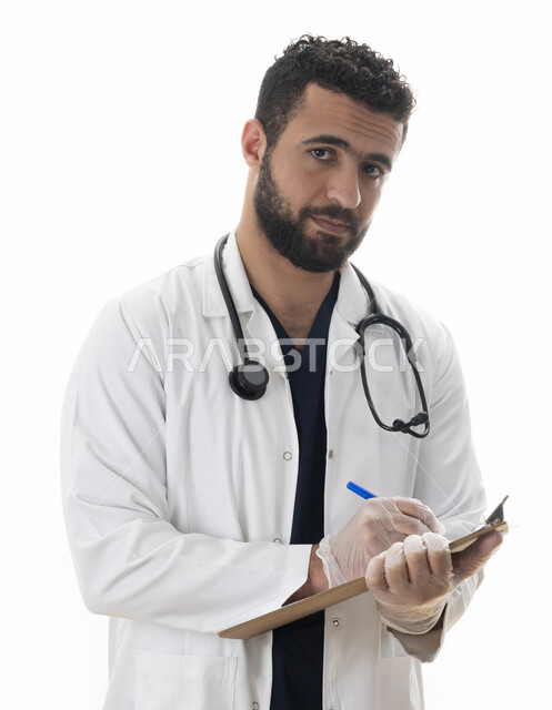 العمل في القطاع الصحي، إعداد التقارير الطبية ,بورتريه لطبيب سعودي يقوم بتدوين نتائج الفحوصات الطبية بالسجل الطبي ، شاب عربي اماراتي خليجي يرتدي المعطف الطبي و يقوم بتقديم خدمات العلاج للمرضى بكل كفاءه ، خلفية بيضاء