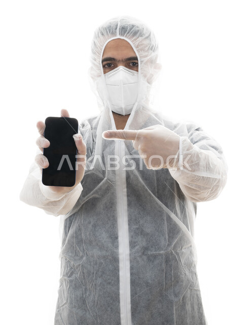 إرتداء اللباس الواقي من فايروس كورونا, بورتريه مقرب لطبيب سعودي يشير بإصبعه على شاشه سوداء فارغه, شاب عربي اماراتي خليجي يتبع توصيات السلامه والوقايه في برامج التوعيه الصحيه في الجوال, تعليمات وزارة الصحة في الالتزام بالاحترازات الوقائيه ضد كوفيد 19