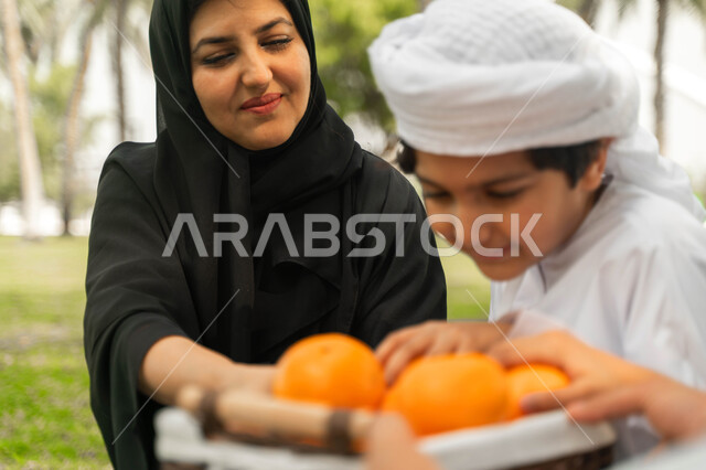 A useful healthy snack, a trip in a spring atmosphere abroad, a local Saudi national product, a family atmosphere full of love, a close-up of an Arab Emirati Gulf family in a park, sharing delicious, fresh and refreshing fruits among family members, a Sau