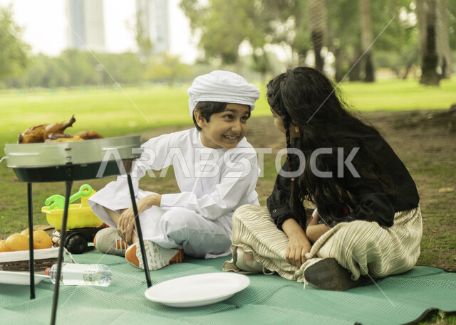 التسامر والضحك بإيماءات تدل على الفرح , مفهوم التعاطف والحب بين الاخوه، انشطة صيفيه ترفيهيه, صورة لبنت عربية اماراتية خليجية تقوم بضم شقيقها يرتدي الكندورة و العمامة البيضاء في إحدى المزارع، ولد وبنت سعوديان في الخارج يستمتعان في التنزه في الهواء الطلق