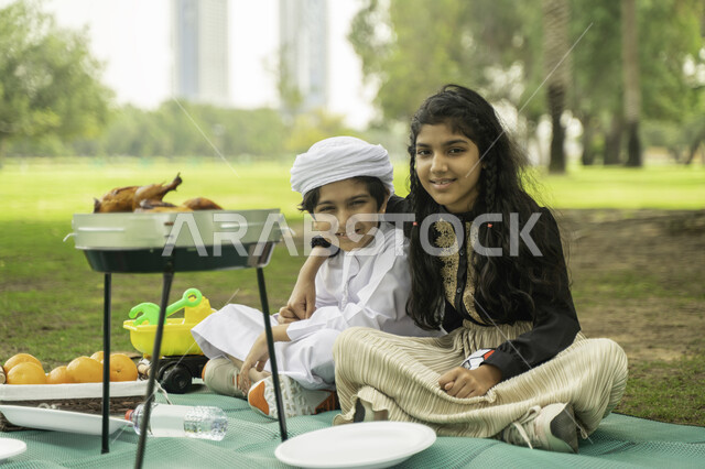 انشطة صيفيه ترفيهيه, ايماءات تدل على الفرح، النظر الى الكاميرا, مفهوم التعاطف والحب بين الاخوه، صورة لبنت عربية اماراتية خليجية تقوم بضم شقيقها يرتدي الكندورة و العمامة البيضاء في إحدى المزارع، ولد وبنت سعوديان في الخارج يستمتعان في التنزه في الهواء الطلق