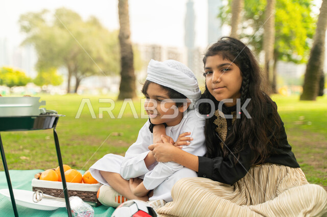 النظر الى الكاميرا, مفهوم التعاطف والحب بين الاخوه، انشطة صيفيه ترفيهيه, صورة لبنت عربية اماراتية خليجية تقوم بضم شقيقها يرتدي الكندورة و العمامة البيضاء في إحدى المزارع، ولد وبنت سعوديان في الخارج يستمتعان بتحضير وجبة الغداء ، نزهه في الهواء الطلق