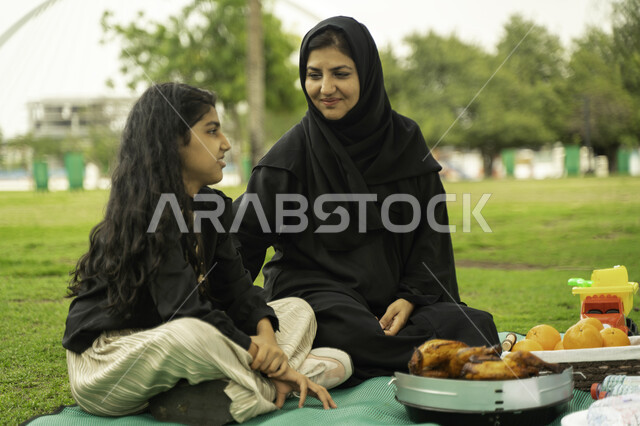 النقاشات والدردشة بين أفراد العائلة، التنزه في الهواء الطلق, أم عربية اماراتية خليجية في احدى الحدائق والمنتزهات مع ابنتها في الخارج, عائلة سعودية تقضي أوقات ممتعه مع الابناء, الاعتناء بالأطفال والاهتمام بهم, انشطة ترفيهيه صيفية، ايماءات تدل على السعادة