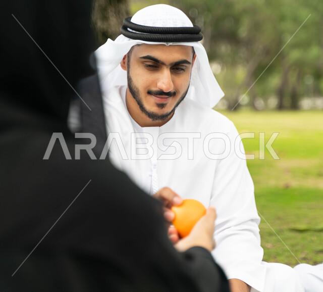 ايماءات تدل على السعادة, منتج سعودي وطني محلي ،سناك مفيد صحي، أجواء عائلية مليئة بالحب، صورة من الخلف لإمرأه عربية اماراتية خليجية تقوم بمشاركة زوجها الفواكه اللذيذة الطازجة المنعشة في إحدى المزارع، عائلة سعودية تقضي أوقات ممتعه في الخارج