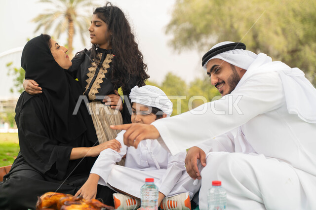 Discussions and chats between family members, referring to something, hiking in the open air, an Arab Emirati Gulf family in one of the gardens and parks abroad, a Saudi family spending fun times with children, taking care of children and taking care of t