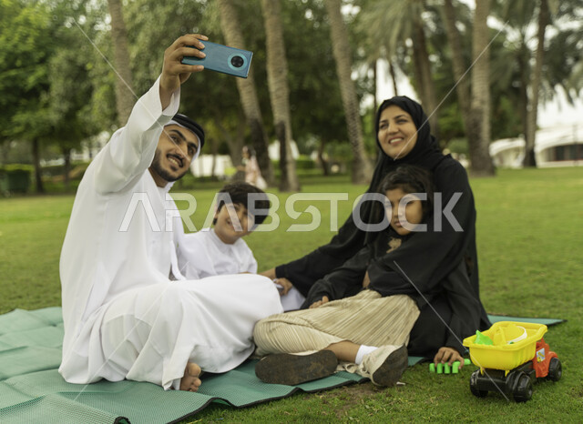 التقاط صور السيلفي للذكريات والتجمعات العائلية الودية عبر الجوال, عائلة عربية اماراتية خليجية في إحدى الحدائق والمنتزهات في الخارج, التنزه في الهواء الطلق, عائلة سعودية تقضي أوقات ممتعه مع الابناء, الاعتناء بالأطفال والاهتمام بهم, انشطة ترفيهيه صيفيه