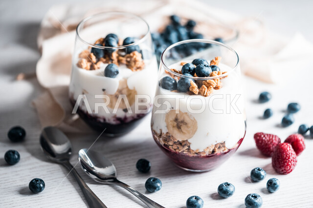 Delicious sweet cups, yogurt with cranberries and strawberries, scattered fruit pieces, sugars, glass cups, delicious dessert with nuts and fruits