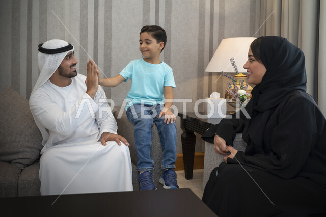 التسامر والضحك بايماءات تدل على الفرح والسعاده، إحترام وتقدير الوالدين، عائله عربيه خليجيه اماراتيه تستمتع بتبادل الاحاديث، اسره سعوديه تجلس في غرفه المعيشه، الحفاظ على الترابط والتواصل بين الأباء والأبناء، أجواء عائليه مليئه بالحب.
