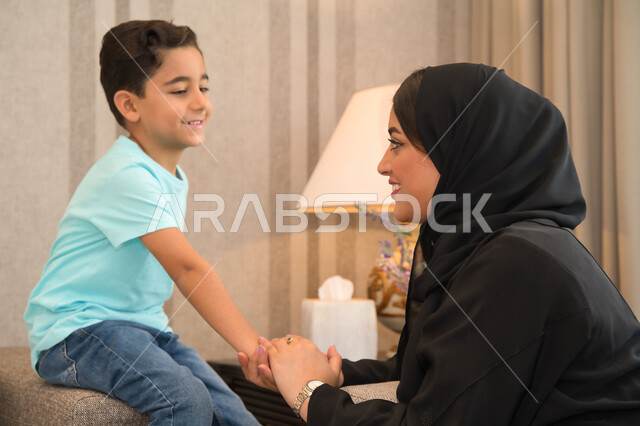 مفهوم التربيه الصالحه للأبناء، مشاركه الأطفال الدردشات والحوارات، أم عربيه خليجيه اماراتيه محجبه ترتدي عباءه سوداء تقوم بالتحدث مع ابنها، ولد عربي سعودي ينظر إلى والدته بحب واهتمام، الحفاظ على الترابط الأسري، الاحساس بالأمان بوجود الأهل.