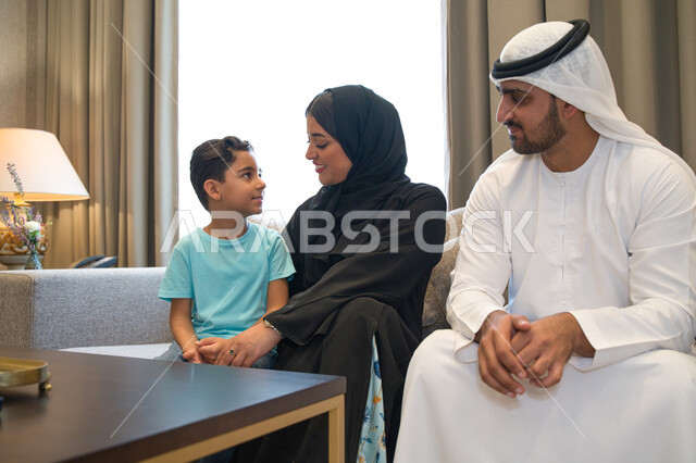 The concept of a happy Saudi family, children’s participation in decision-making, a Saudi Gulf Arab family sitting in the living room chatting and dialogues, expressions indicating joy and happiness to spend time with the family, asking permission and asking the family with respect and politeness.