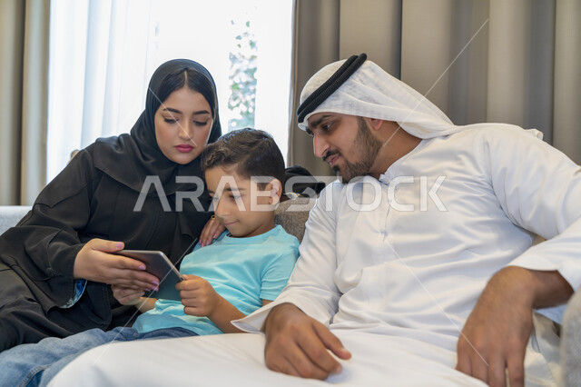 قضاء أوقات مليئه بالحب والموده، عائله عربيه خليجيه اماراتيه تجلس في غرفه المعيشه، أسرة سعوديه تقوم بمشاهدة المسلسلات الممتعه عبر جهاز التابلت، متابعه مواقع التواصل الاجتماعي، استخدام الأجهزة الالكترونيه والتقنيات الحديثه، أجواء عائليه منزليه هادئه.
