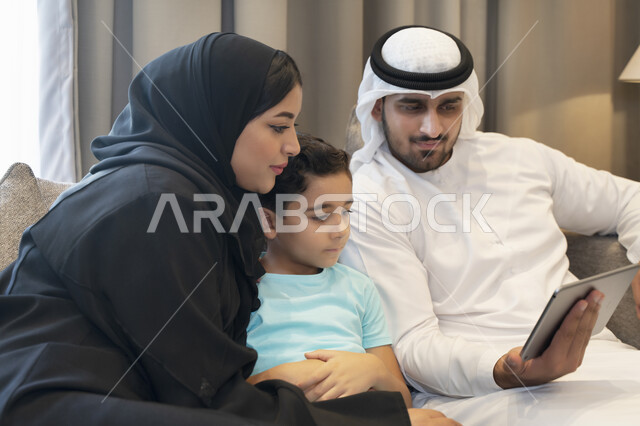 استخدام الأجهزة الالكترونيه والتقنيات الحديثه، أجواء عائليه منزليه هادئه، عائله عربيه خليجيه اماراتيه تجلس في غرفه المعيشه، أسرة سعوديه تقوم بمشاهدة المسلسلات الممتعه عبر جهاز التابلت، متابعه مواقع التواصل الاجتماعي، قضاء أوقات مليئه بالحب والموده.