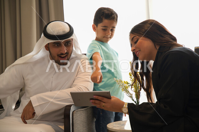 الاشارة إلى شيء ما ومتابعة مواقع التواصل الاجتماعي، الجلوس في غرفة المعيشة وقضاء أجواء ممتعه مع الأبناء، عائلة عربية خليجية إماراتية مبتسمة تقوم بالتسوق الاونلاين عبر جهاز التابليت، أسرة سعودية تقوم بنقاشات وحوارات عائلية حول التسويق الالكتروني المنزلي 