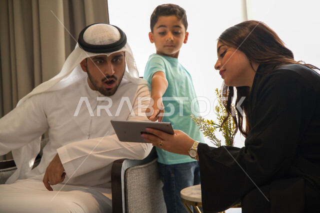 ايماءات تدل على الدهشة والاشارة إلى شيء ما، الجلوس في غرفة المعيشة وقضاء أجواء ممتعه مع الأبناء، عائلة عربية خليجية إماراتية تقوم بالتسوق الاونلاين عبر جهاز التابليت، أسرة سعودية تقوم بنقاشات وحوارات عائلية حول التسويق الالكتروني المنزلي 