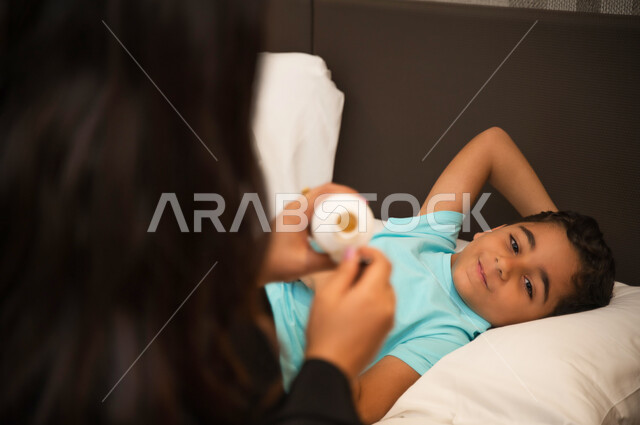 الثقة بحنان الأم ودورها في حياة الأبناء, الالتزام بالأوقات الصحيحة لتناول الدواء وأخذه بصورة آمنة, صورة مقربة لولد عربي خليجي إماراتي يمر بحالة من المرض وينظر لوالدته, أم سعودية تعطي ابنها المريض الشراب المناسب