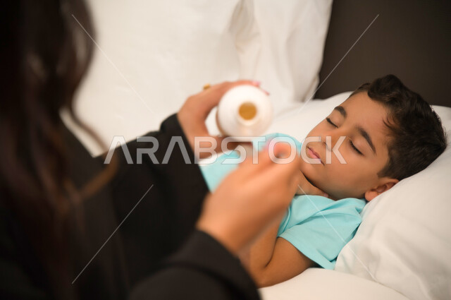 Commitment to the correct times for taking medicine and taking it safely, a close-up of a sleeping Arab Gulf Emirati child going through a state of illness, a Saudi mother giving her sick son the appropriate drink, the suffering of children during their i