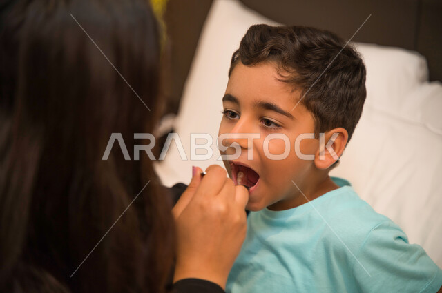 اهتمام الوالدين بأبنائهم, أهمية استخدام الدواء بوصفة طبية والالتزام بالعلاج الدوائي, صورة مقربة لولد عربي خليجي إماراتي يمر بحالة من المرض يستلقي على السرير, أم سعودية تعطي الشراب المناسب لطفلها المريض, الانتظام بتناول الدواء في الأوقات المحددة