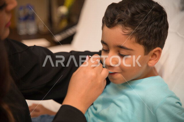The importance of using medicine according to a medical prescription and adherence to drug treatment, a close-up of an Arab Gulf Emirati child who is going through a state of illness lying on the bed, a Saudi mother giving the appropriate drink to her sic