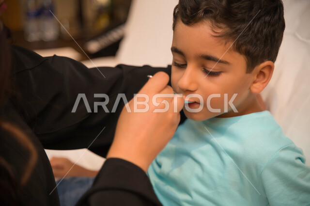 الالتزام بالعلاج الدوائي وأهمية استخدام الدواء بوصفة طبية, صورة مقربة لولد عربي خليجي إماراتي يمر بحالة من المرض يستلقي على السرير, أم سعودية تعطي الشراب المناسب لطفلها المريض, الانتظام بتناول الدواء في الأوقات المحددة, اهتمام الوالدين بأبنائهم