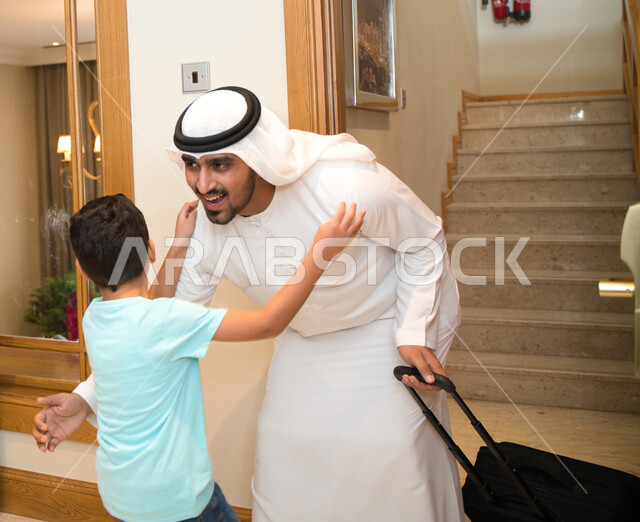 دور الأب في حياة الابناء، ايماءات تدل على الحماس والسعاده، رجل عربي خليجي اماراتي يرتدي الزي التقليدي يمسك بيده حقيبه سفر، صبي سعودي يقوم بإحتضان والده، بناء علاقة قويه مع الأولاد، فرحة العوده من السفر والإجتماع مع العائله.