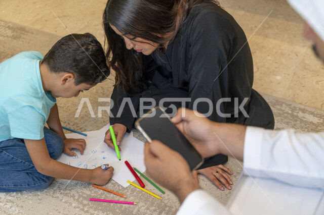 قضاء أوقات ممتعه في المنزل، تنمية المهارات الفكريه لدى الأطفال، أم عربيه خليجيه إماراتيه تقوم بالرسم والتلوين مع ابنها، صوره مقربه ليد أب سعودي يقوم بإلتقاط صور تذكاريه، الرعايه والإهتمام بتربيه وتعليم الأبناء، مشاركه الأولاد الأنشطه التعليميه المفيده.