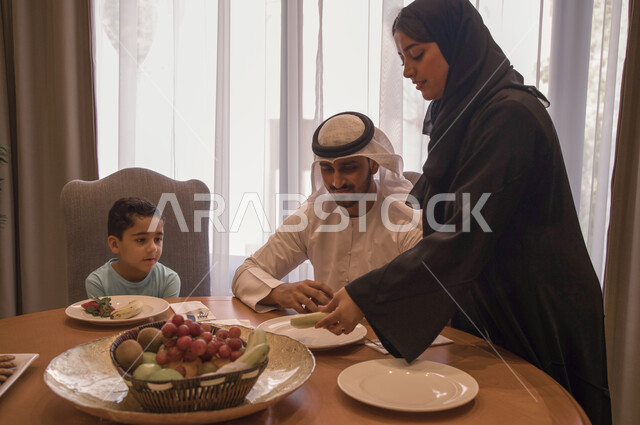 منتجات محليه وطنيه سعوديه، صحن من الفواكه الطازجة المفيده والشهيه، عائله عربيه خليجيه اماراتيه تجلس على طاوله طعام مليئه بالسناكات الصحيه الخفيفه، امرأه سعوديه تقدم الفاكهة المنعشه لأسرتها، جلسات عائليه هادئه وممتعه, البركه في الإجتماع على المائده.