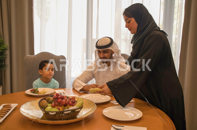 جلسات عائليه هادئه وممتعه, طبق من الفواكه الطازجة المفيده والشهيه، عائله عربيه خليجيه اماراتيه تجلس على طاوله طعام مليئه بالسناكات الصحيه الخفيفه، امرأه سعوديه تقدم الفاكهة المنعشه لأسرتها، منتجات محليه وطنيه سعوديه، البركه في الإجتماع على المائده.