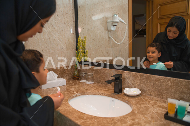 تجنب تسوس الأسنان وأمراض اللثه، مفهوم الإهتمام بالنظافه الشخصيه وصحه الأسنان، إمرأه عربيه خليجية اماراتيه تساعد ابنها في تنظيف أسنانه والعنايه بها، ولد سعودي وأمه يقفان عند المغسله، الرعايه الصحيه للأطفال، روتين نظافه الفم اليوميه.