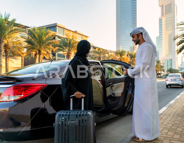 Passenger delivery service to and from the airport, an Arab Emirati man wearing a kandora and a ghutra opens the car door for a veiled Saudi woman wearing a black abaya holding a travel bag in her hand, convenient and safe transportation services, the con