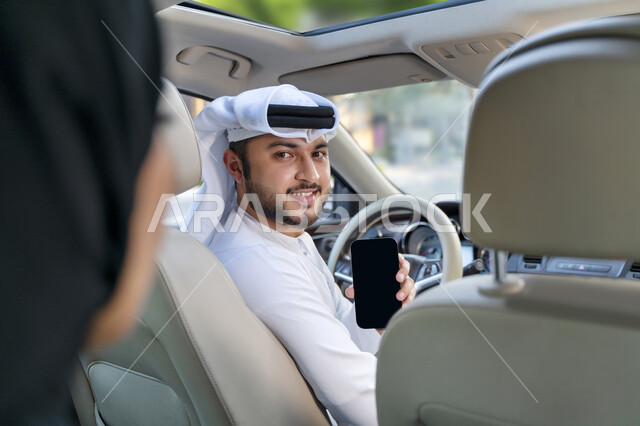 Request for transportation service through the electronic delivery application, an Arab Gulf Emirati driver working in a taxi, a veiled Saudi Gulf Arab woman holding a mobile phone in her hand, a Saudi man delivering the passenger to her desired destinati