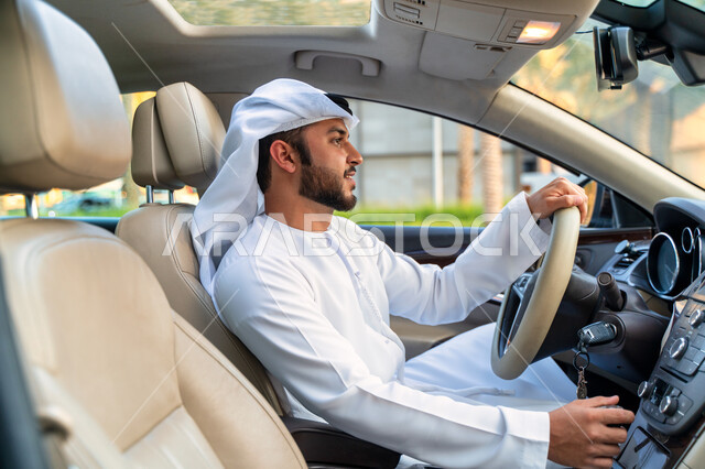A man's mastery of driving a car in public roads and streets, a side view of an Emirati Arab Gulf youth sitting inside his car, the concept of freedom, independence and self-reliance, a Saudi youth wearing a kandora and ghutra looking at something, drivin