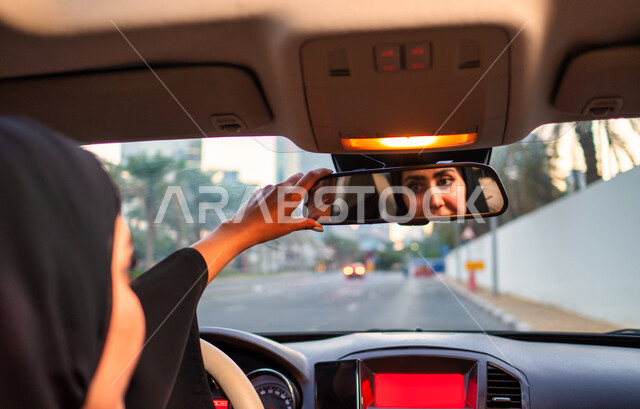 تعديل مرآة الرؤية الخلفية للسيارة، انعكاس صورة سائقة عربية إماراتية خليجية محجبة في مرآه السيارة، مفهوم الاستقلال و الحرية و الاعتماد على النفس، حرية القيادة للمرأة العربية، سيده سعودية ترتدي العباءة السوداء، اتباع قواعد السلامة