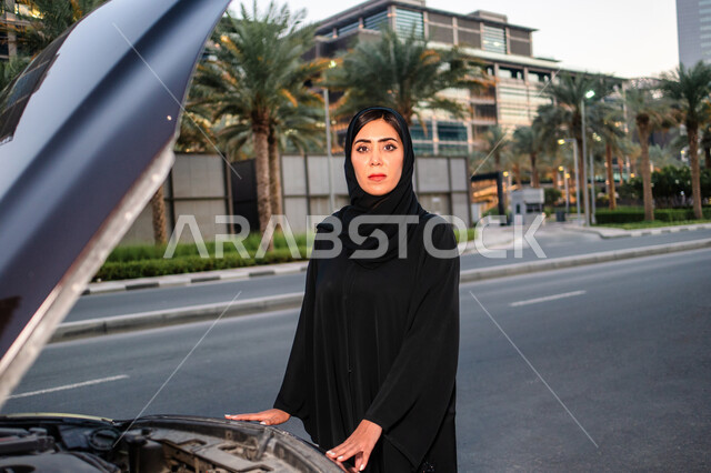 Inspection and repair of the car, the concept of independence, freedom and self-reliance, a veiled Emirati Arab Gulf woman standing near her broken car with the hood open, freedom of driving for Arab women, a Saudi woman wearing the abaya, women’s self-re