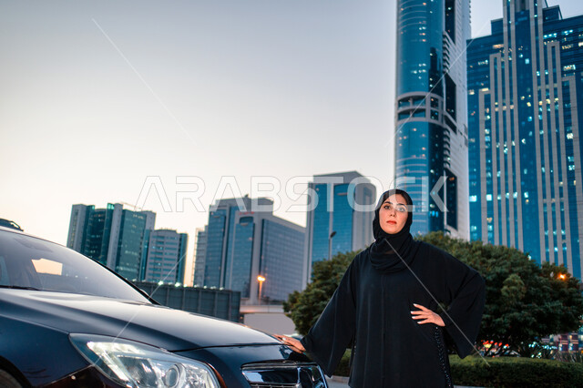 حرية القيادة للمرأة العربيه، مفهوم الاستقلال و الحرية و الاعتماد على النفس، إمرأه عربية خليجية إماراتيه محجبة تقف بالقرب من سيارتها، إيماءات الوقوف بثقة، النظر والتفكير في شيء ما، سيده سعودية ترتدي العباءة السوداء، خلفية أبراج ومباني مدينة دبي
