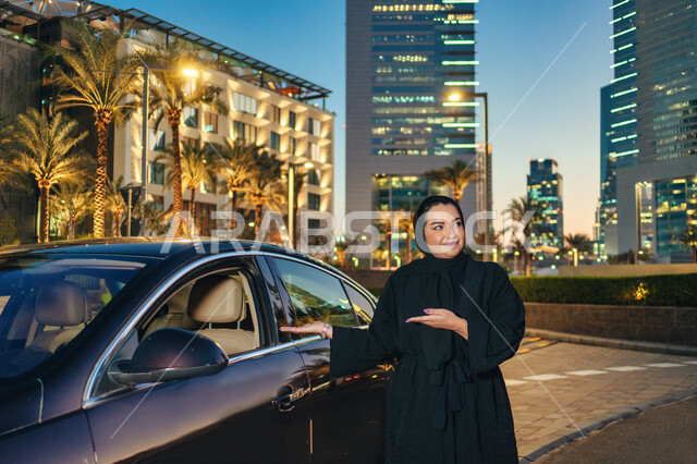 ايماءات يدين تدل على الاشارة لداخل السياره، حرية القيادة للمرأة العربية، سيده سعودية تشير بيديها الى السيارة، اعتماد المرأه على نفسها في التنقل و المواصلات, مفهوم الاستقلال و الحرية و الاعتماد على النفس، امرأه عربية خليجية اماراتيه محجبة ترتدي العباءة تقف
