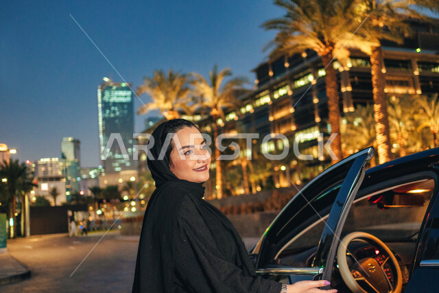 الاستعداد لركوب السياره، سيده سعودية ترتدي العباءة تقوم بفتح باب السيارة، اعتماد المرأه على نفسها في التنقل و المواصلات, مفهوم الاستقلال و الحرية و الاعتماد على النفس، امرأه عربية خليجية اماراتيه محجبة تقف بجانب سيارتها، حرية القيادة للمرأة العربية.