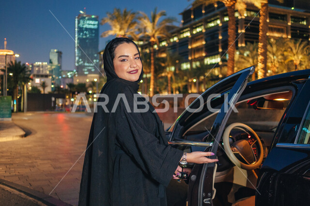 مفهوم الاستقلال و الحرية و الاعتماد على النفس، امرأه عربية خليجية اماراتيه محجبة تقف بجانب سيارتها، حرية القيادة للمرأة العربية، سيده سعودية ترتدي العباءة تقوم بفتح باب السيارة، اعتماد المرأه على نفسها في التنقل و المواصلات، الاستعداد لركوب السياره.