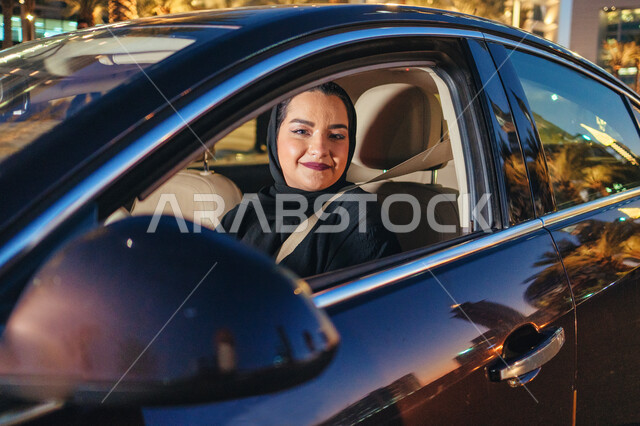 الإلتزام بقواعد الحركة المرورية، إتقان قيادة المرأة للسيارة في الطرق الرئيسية، سيدة عربية اماراتيه خليجية مبتسمة تجلس داخل سيارتها، مفهوم الاستقلال والاعتماد الذاتي ، شابة سعودية محجبة ترتدي حزام الأمان وتقود بحذر، اتباع قوانين الأمن والسلامة العامة.