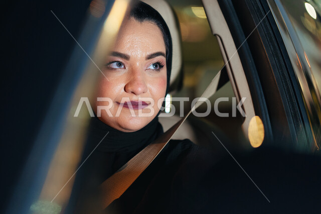 شابة سعودية محجبة ترتدي حزام الأمان وتقود بحذر، اتباع قوانين الحركة المرورية، إتقان قيادة المرأة للسيارة في الطرق الرئيسية، سيدة عربية اماراتيه خليجية تجلس داخل سيارتها تنظر لشيء ما، مفهوم الاستقلال والاعتماد الذاتي، الإلتزام بقواعد الأمن والسلامة العامة.